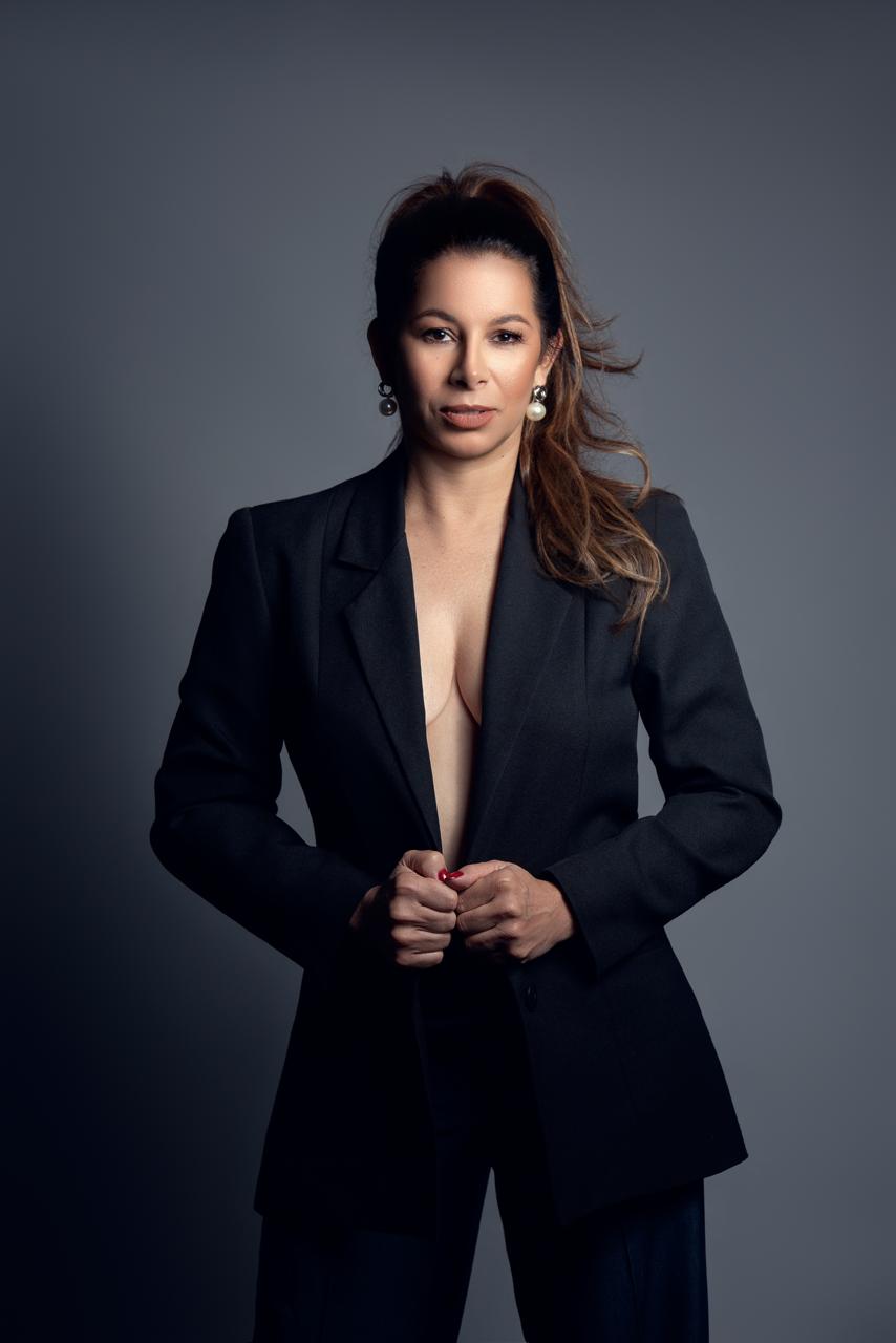 Simara Pires de blazer preto aberto, sobre fundo cinza